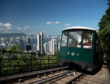A  green Peak Tram ascending the picturesque hills of Hong Kong, providing a scenic ride to the highest point on Hong Kong Island. Passengers aboard are treated to awe-inspiring panoramic views of the city skyline and Victoria Harbour.