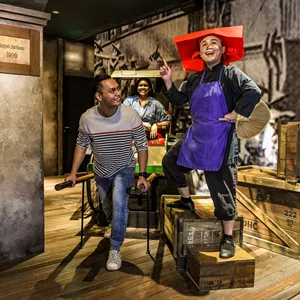 A set up of Singapore's history in the 1900s, depicting Keppel Harbour. A realistic wax figure of a Samsui woman beams as she stands on two boxes. A happy man holds the handles of the rickshaw and acts like he is pulling it with a girl seated behind.