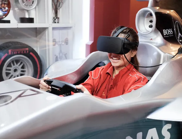 Virtual reality racing experience at Madame Tussauds Singapore - A person wearing a VR headset sitting in a racing seat with a steering wheel and pedals