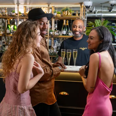Three guests standing at the bar at Madame Tussauds London's 1835 Champagne Bar, enjoying drinks in a stylish setting.