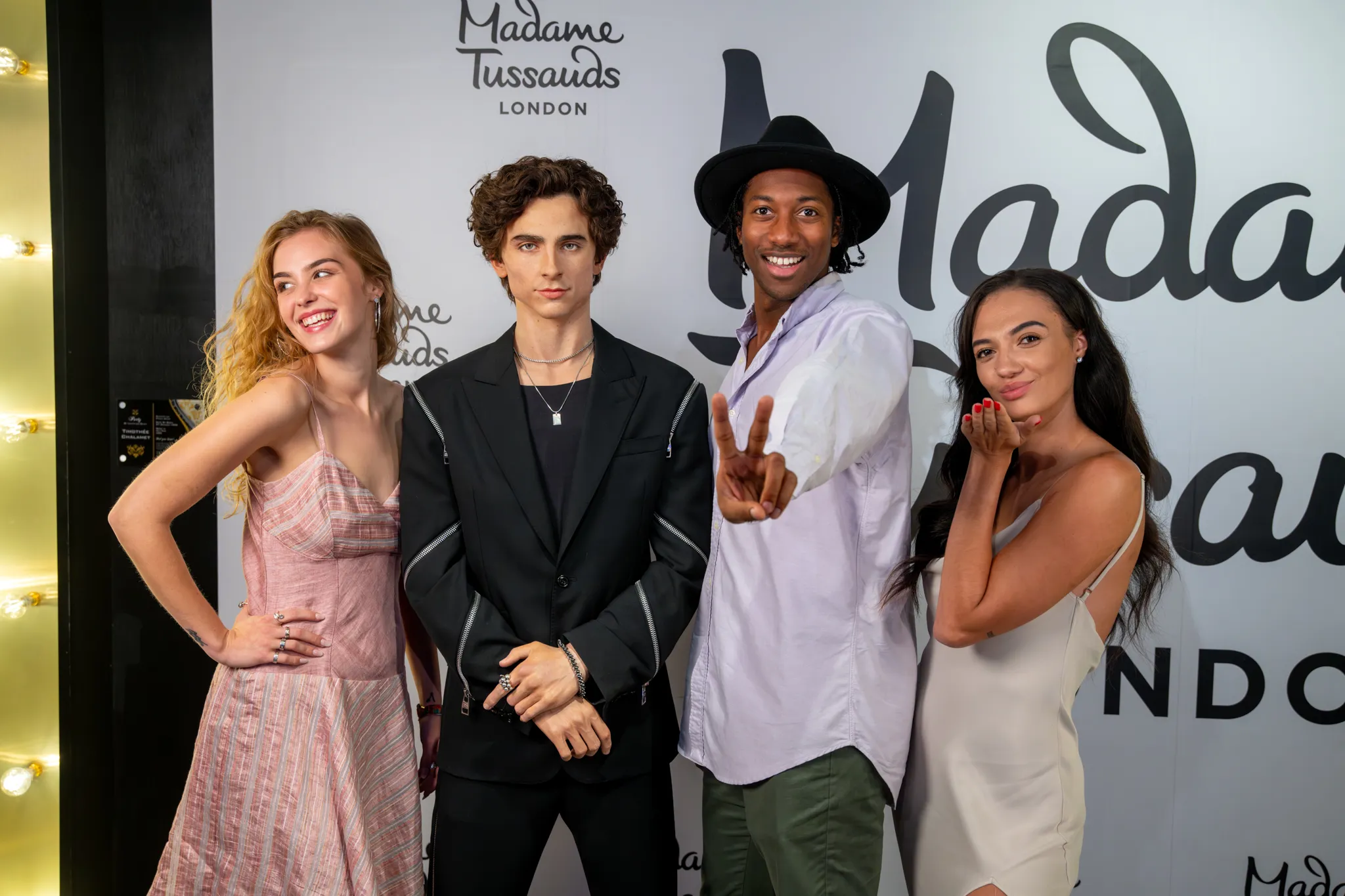 Three people standing with a figure of Timotheé Chalamet in an awards red carpet setting