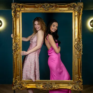 Two guests posing inside a large photo frame at Madame Tussauds London's 1835 Champagne Bar, smiling in an elegant setting.