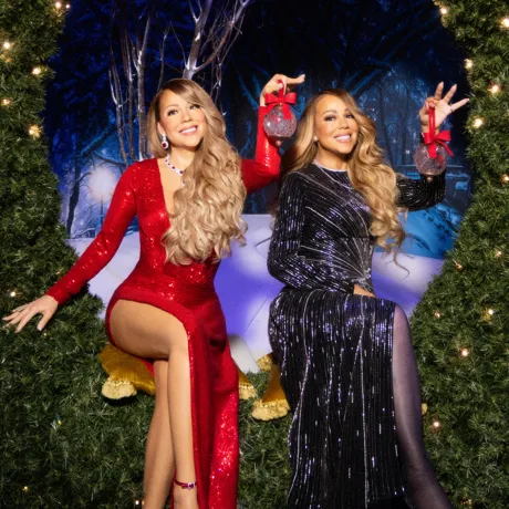 Mariah Carey sitting on a wreath holding an ornament next to her wax Mariah Carey in the same pose