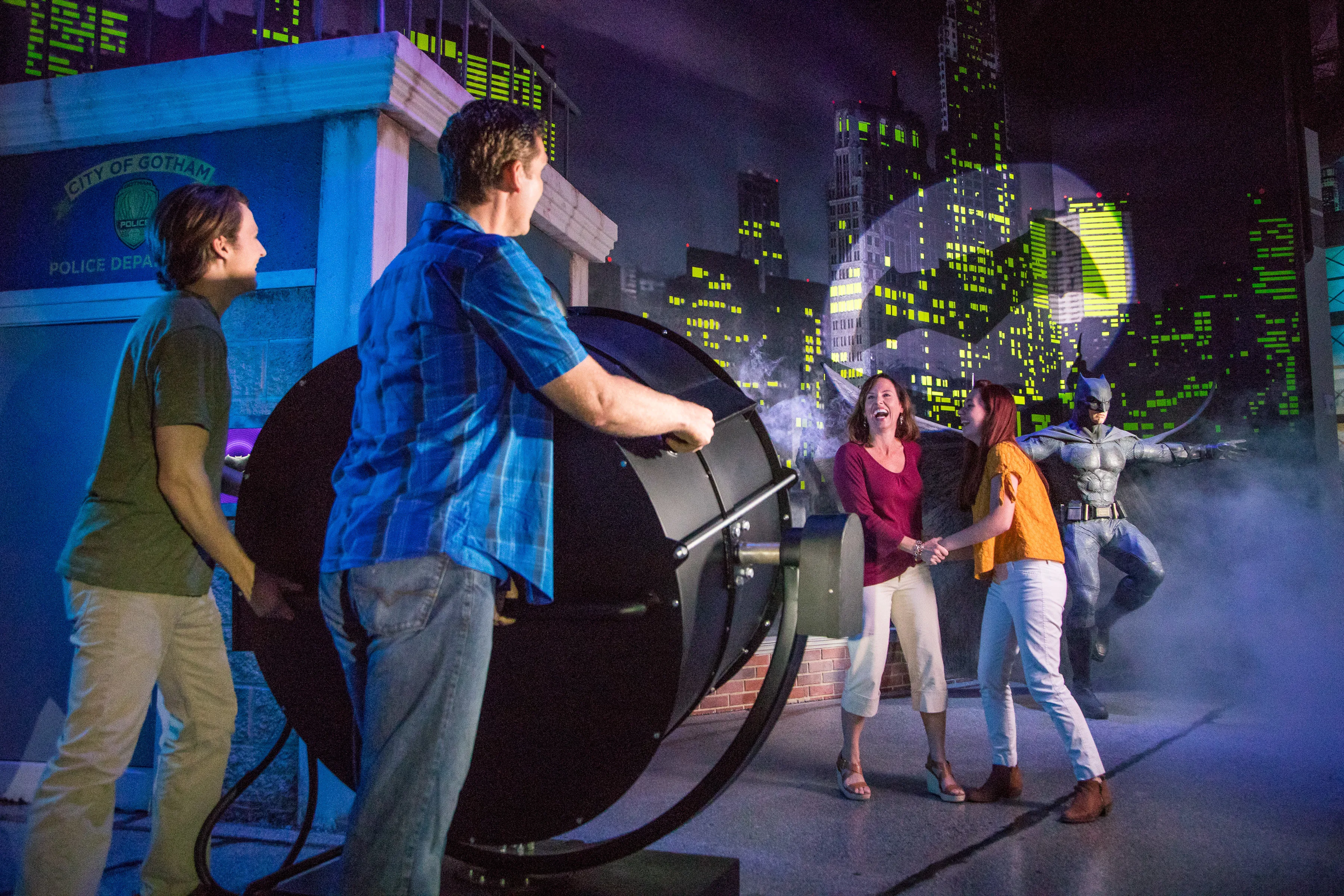 Four guests interact with the Bat-Signal in front of the Batman wax figure at Madame Tussauds Orlando.