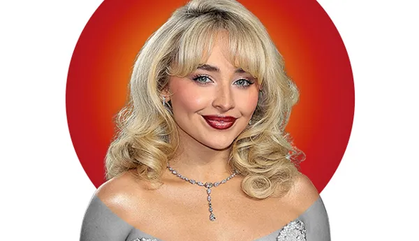 Portrait of singer Sabrina Carpenter with blonde wavy hair, wearing a low-cut dress with a diamond necklace. A vibrant red and orange circular background highlights her face. Featured in Madame Tussauds' 'Hot 100' list.