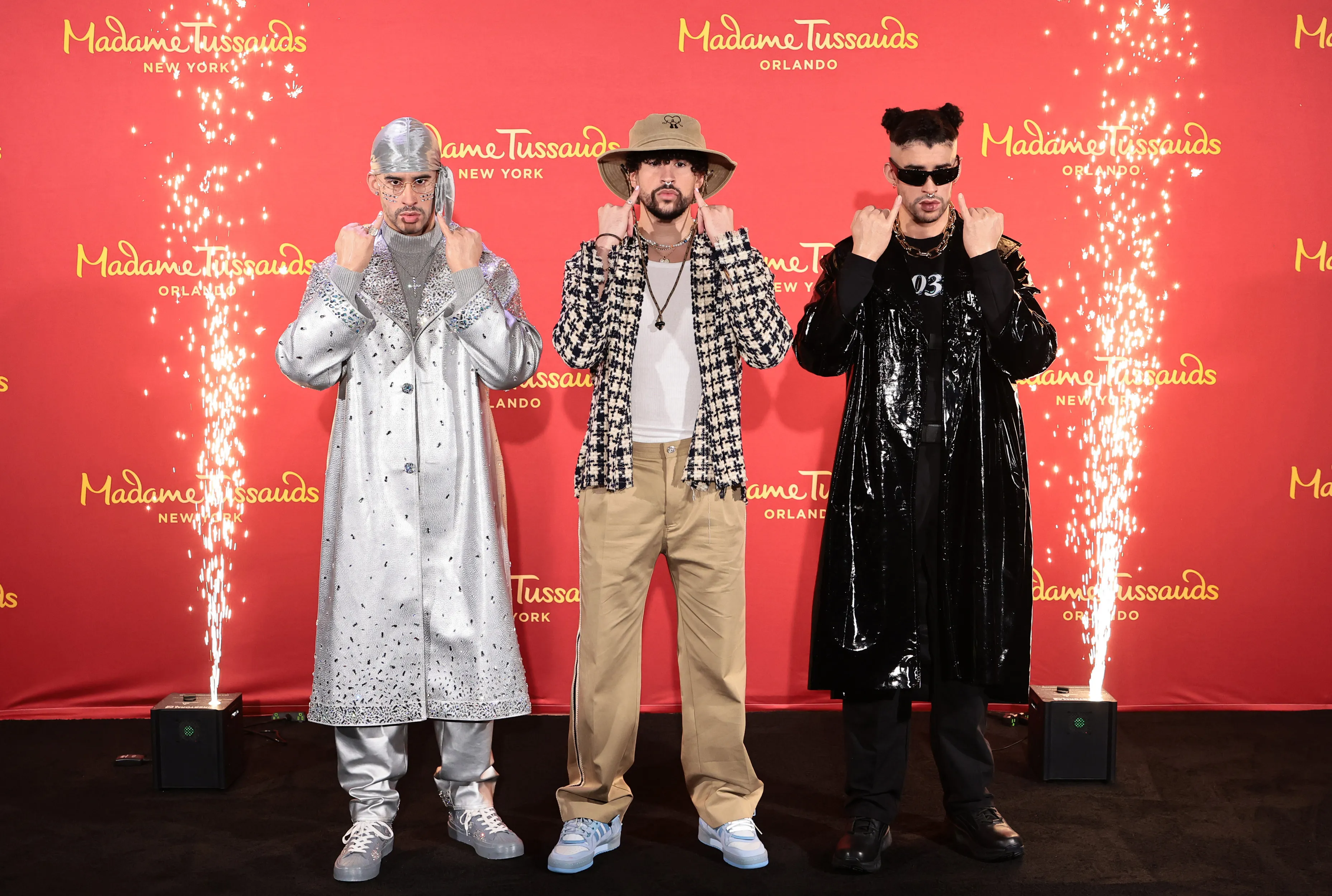 Bad Bunny poses next to his two wax figures, mirroring their expressions and gestures.