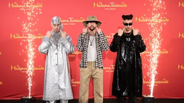 Bad Bunny poses next to his two wax figures, mirroring their expressions and gestures.