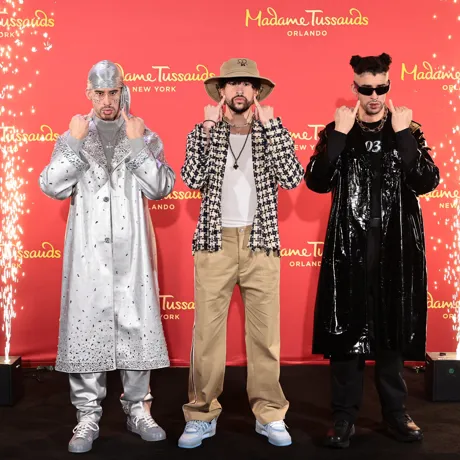 Bad Bunny poses next to his two wax figures, mirroring their expressions and gestures.