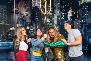 Three guests pose with Justice League’s Aquaman wax figure at Madame Tussauds Orlando, smiling excitedly.