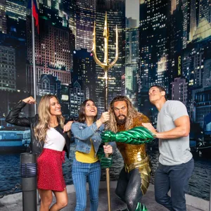 Three guests pose with Justice League’s Aquaman wax figure at Madame Tussauds Orlando, smiling excitedly.