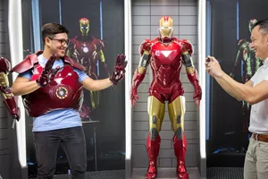 A visitor at Madame Tussauds Singapore - Marvel Universe 4D trying on the Iron Man suit exhibit. The visitor is standing in front of a display of other Iron Man suits and props