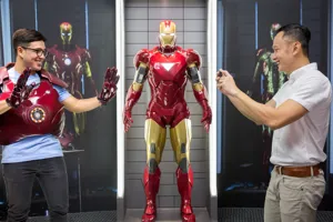 A visitor at Madame Tussauds Singapore - Marvel Universe 4D trying on the Iron Man suit exhibit. The visitor is standing in front of a display of other Iron Man suits and props