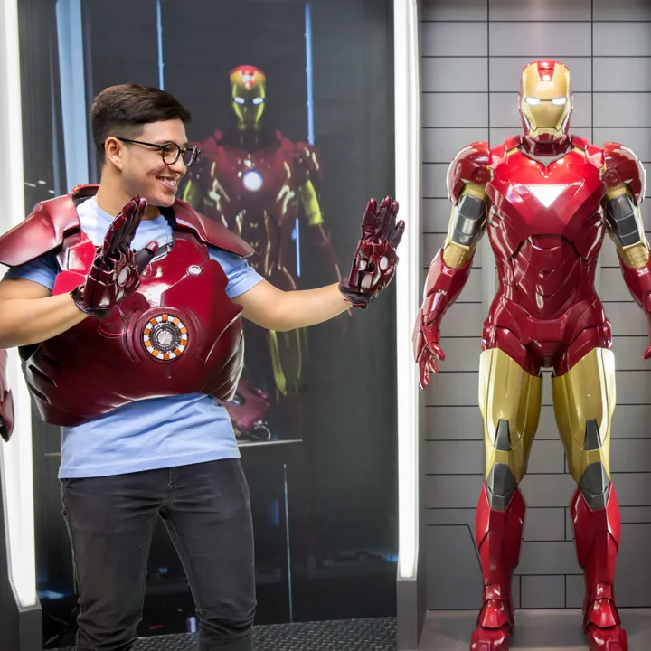 A visitor at Madame Tussauds Singapore - Marvel Universe 4D trying on the Iron Man suit exhibit. The visitor is standing in front of a display of other Iron Man suits and props