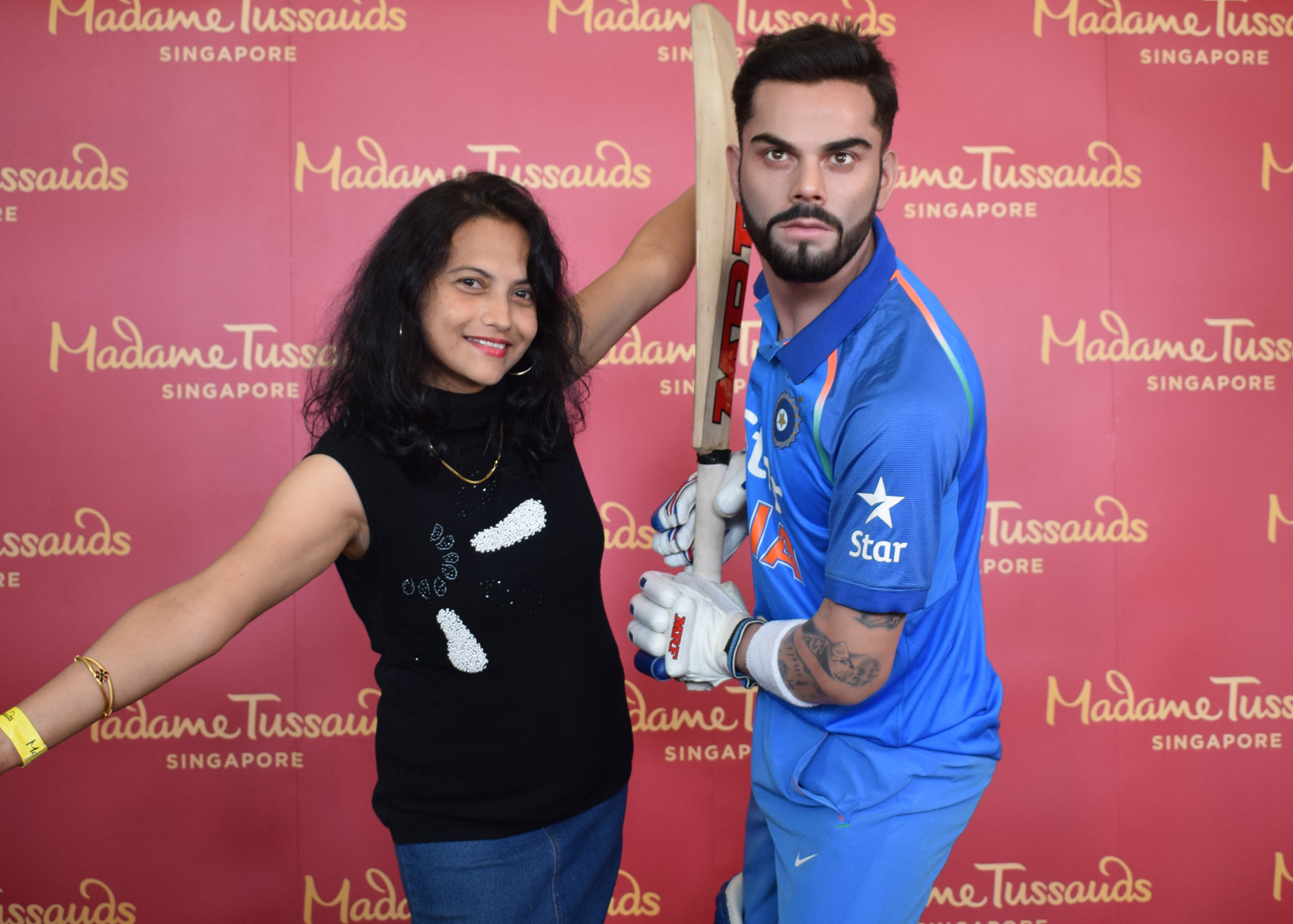  A female visitor poses with open arms beside Virat Kohli, one of India's best cricket player's wax figure in Madame Tussauds. The wax figure is in a batting stance with a bat in his hands and has a serious look.
