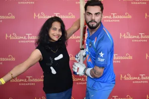 A female visitor poses with open arms beside Virat Kohli, one of India's best cricket player's wax figure in Madame Tussauds. The wax figure is in a batting stance with a bat in his hands and has a serious look.