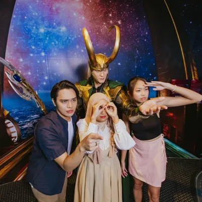 Three Madame Tussauds Singapore visitors are taking fun pictures with a wax figure of Loki from Marvel, indicating that they purchased their tickets at a lower price with fantastic discount promos, ensuring a rewarding and enjoyable experience.