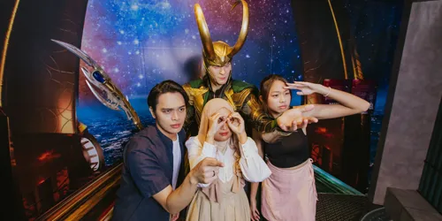 Three Madame Tussauds Singapore visitors are taking fun pictures with a wax figure of Loki from Marvel, indicating that they purchased their tickets at a lower price with fantastic discount promos, ensuring a rewarding and enjoyable experience.