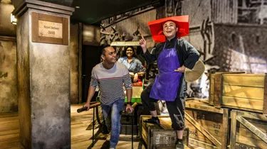 A set up of Singapore's history in the 1900s, depicting Keppel Harbour. A realistic wax figure of a Samsui woman beams as she stands on two boxes. A happy man holds the handles of the rickshaw and acts like he is pulling it with a girl seated behind.