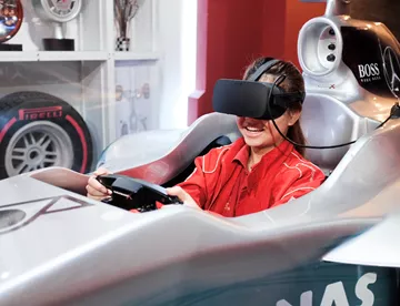 Virtual reality racing experience at Madame Tussauds Singapore - A person wearing a VR headset sitting in a racing seat with a steering wheel and pedals