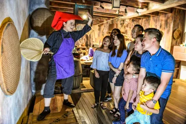 A group of adults and kids standing in awe with a smile on their face, seeing a Madame Tussauds Singapore staff explaining something in a samsui women costume.
