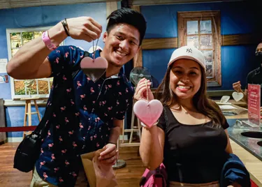 Two people holding a heart-shaped wax that's hanging on a brown thread, as part of wax dipping workshop in Madame Tussauds Singapore